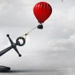 A large anchor holding a red hot air balloon over water.